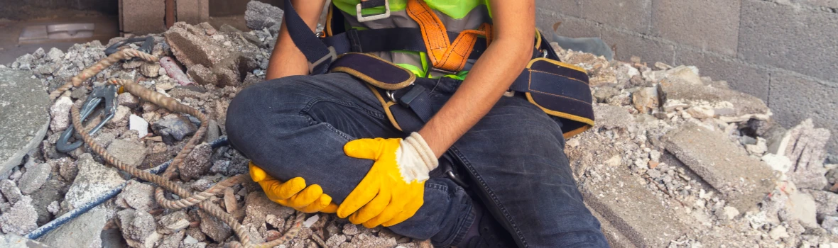 Mann sitzt auf Bauschutt und hält seinen Unterschenkel fest