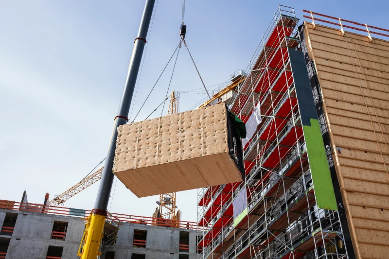 Kran verteilt fertige Holzbauteile auf einer Baustelle