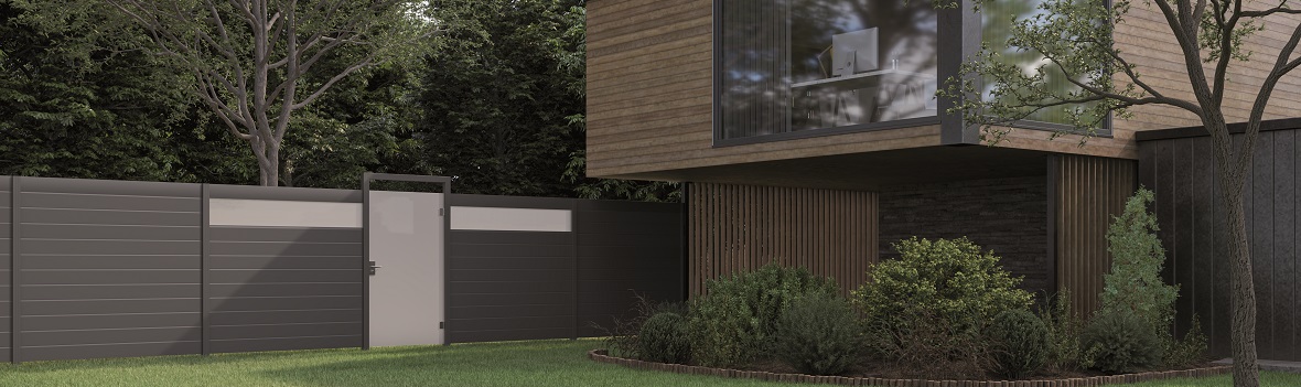 Ein anthrazit-farbender Zaun begrenzt einen Garten. Rechts steht ein Haus mit Holzfront.