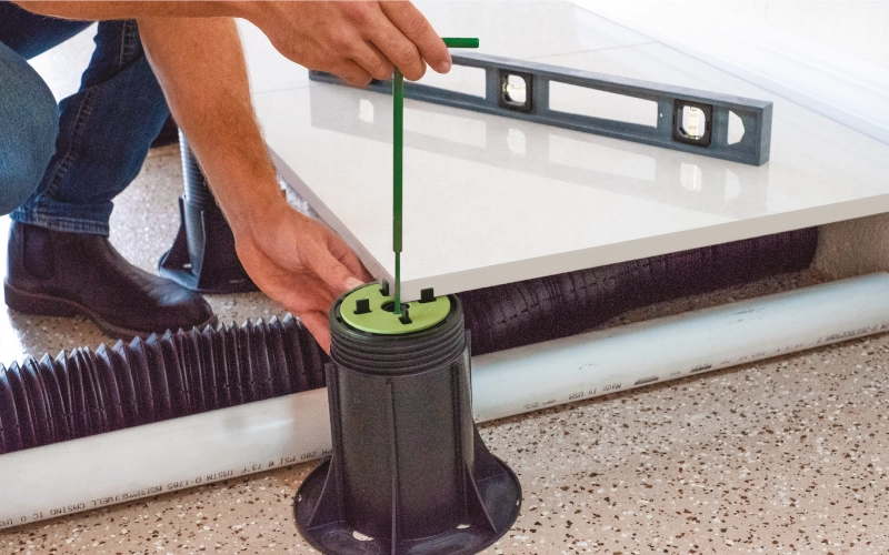 Monteur verstellt die Höhe eines Stelzlagers und richtet eine Terrassenfliese mit einer Wasserwaage aus.