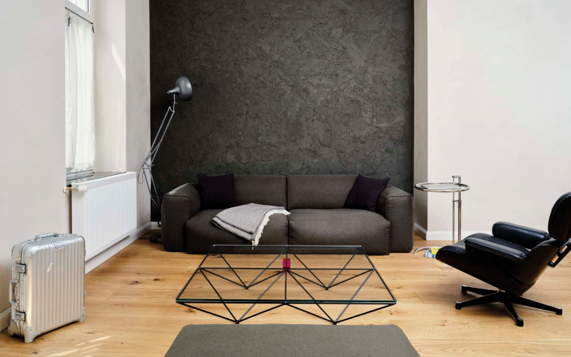Modernes Wohnzimmer mit dunkler Akzentwand, grauem Sofa, Glas-Couchtisch und Ledersessel.