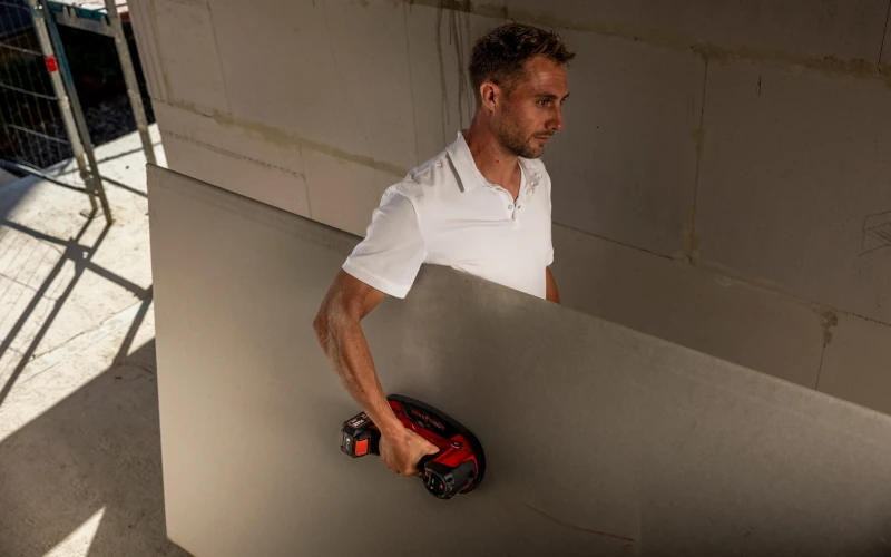 Handwerker transportiert eine Bodenplatte mit Vakuumheber von Flex in der Hand 