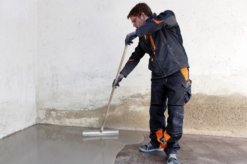 Ein Arbeiter verteilt flüssigen Beton mit einem Abziehgerät auf dem Boden.
