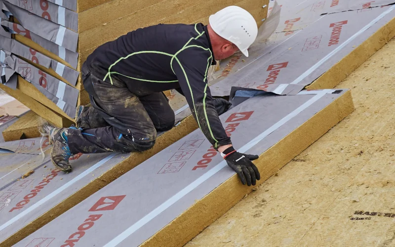 Arbeiter in Schutzkleidung legt Dämmplatte auf einem Dach aus