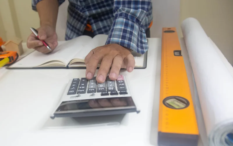 Handwerker tippt auf dem Taschenrechner mit einem Notizbuch daneben
