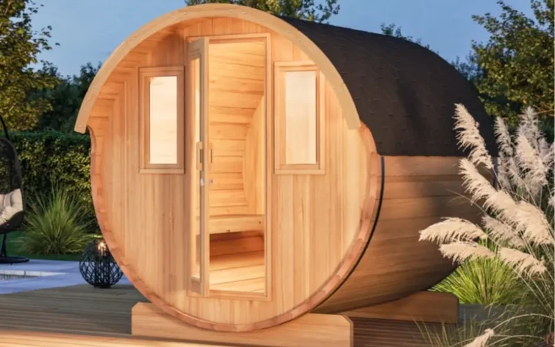 eine runde Fassauna auf Stelzen mit Beleuchtung auf einer Terrasse