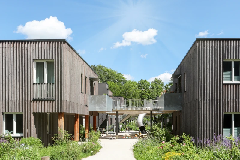 Moderne Mehrfamilienhäuser in Holzbauweise mit üppiger Grünanlage.