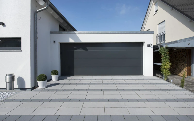 Außenbereich eines Wohnhauses mit hellgrauen Bodenplatten und Garage