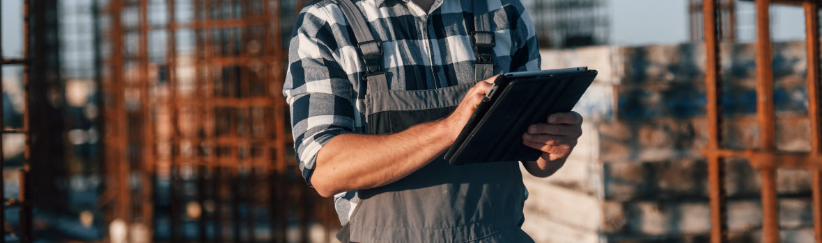 Bauarbeiter mit Tablet auf Baustelle, Metallgerüste im Hintergrund.
