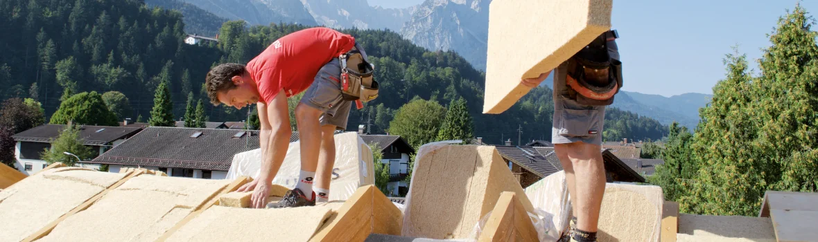 zwei Männer arbeiten auf einem Dach und legen dieses mit Dämmplatten aus 