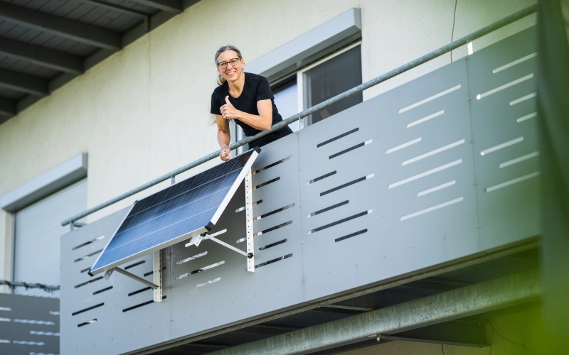 Frau zeigt glücklich den Daumen nach oben, nach Installation eines Solarpanels auf dem Balkon