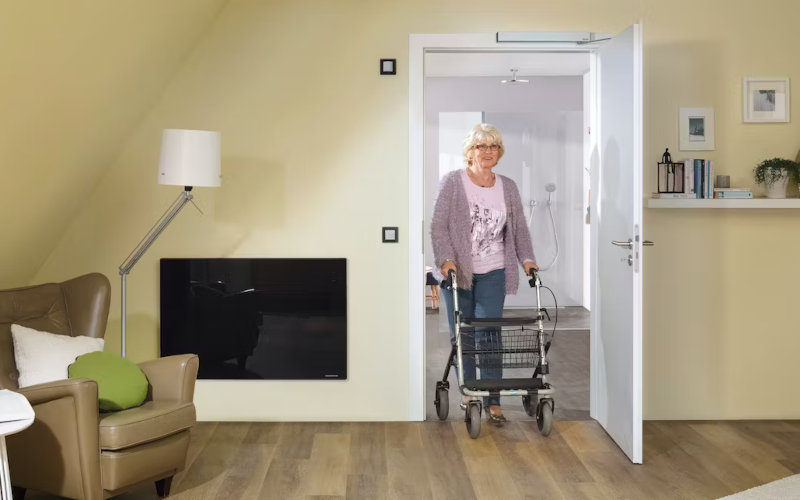 Frau mit Rollator geht durch eine sich automatisch öffnende Zimmertür