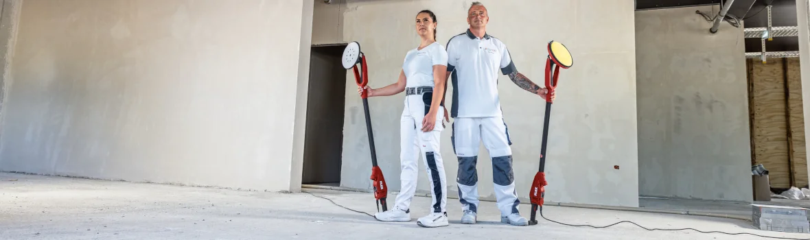 zwei Maler stehen mit FLEX Wand- und Deckenschleifern in der Hand in einem Trockenbau