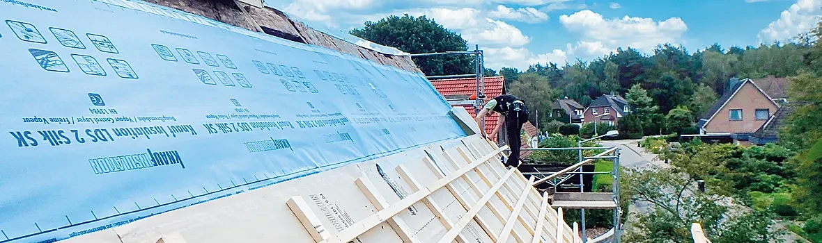 Handwerker befindet sich auf ungedecktem Dach in einem Wohngebiet und baut Dämmung ein.