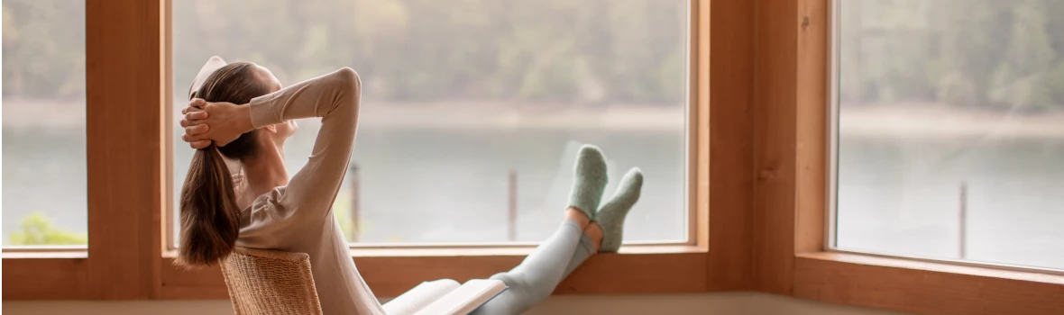Eine Frau auf einem Stuhl schaut aus dem Fenster, auf ein See. 