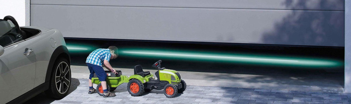 Kind baut Hänger an Spielzeugtraktor vor einem grauen Garagentor von Hörmann 