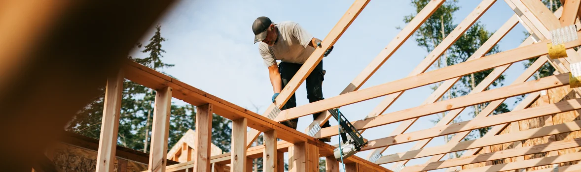 Arbeiter steht auf Dachkonstruktion von einem im Bau befindlichen Haus in Holzrahmenbauweise
