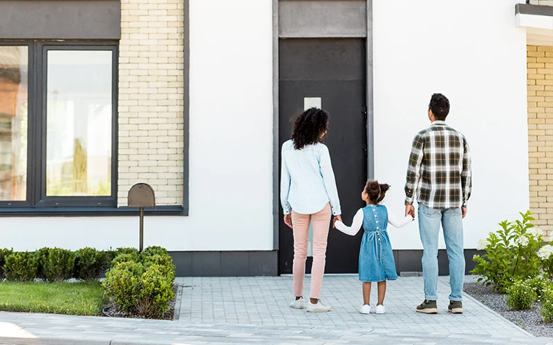 Familie steht vor einem Wohnhaus mit weißer Fassade und schwarzer Haustür