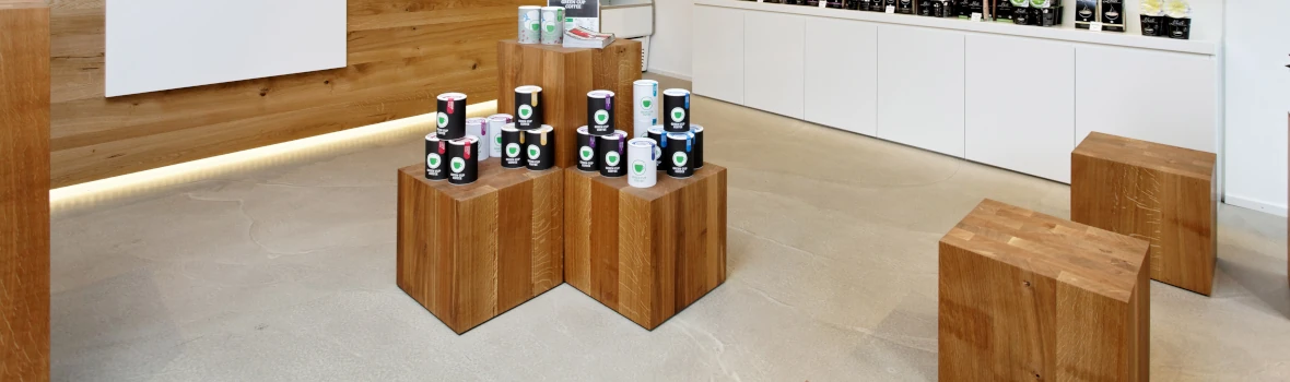 Ein Verkaufsladen mit Produktausstellern aus Holz und einem Verkaufstresen. Der Boden ist in einer Betonoptik.