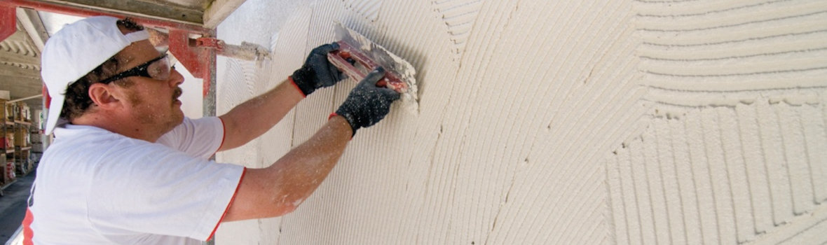 Handwerker verputzt eine Hauswand mit einem Spachtel 