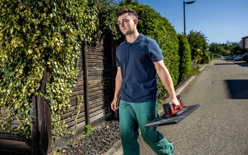 Handwerker transportiert eine Bodenplatte mit Vakuumheber von Flex in der Hand 