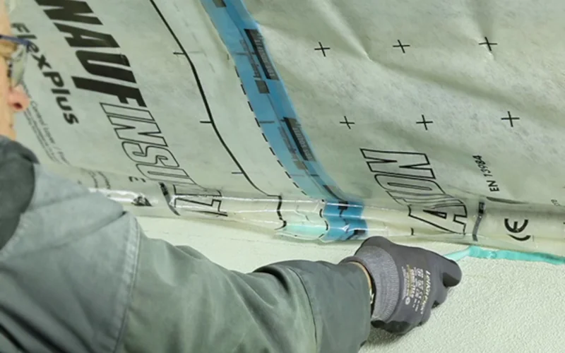 Handwerker klebt Dampfbremsfolie mit Kleber an der Wand an