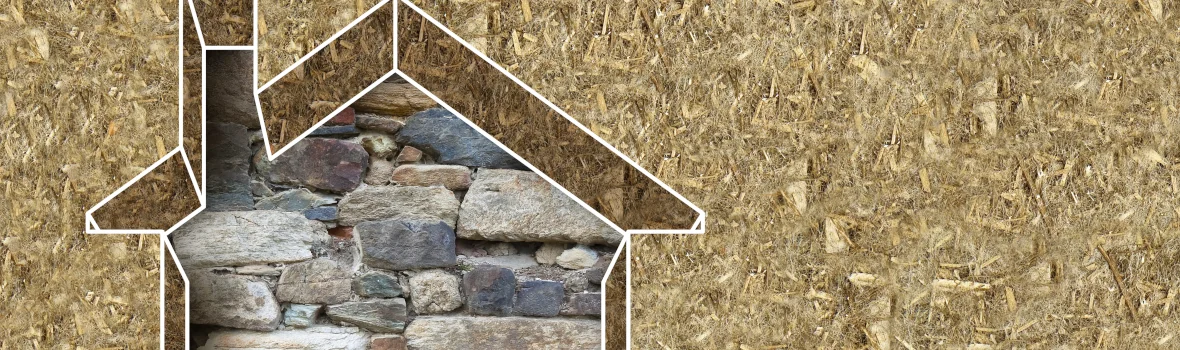 Haus aus einer Hanfwand ausgeschnitten dahinter eine Steinmauer