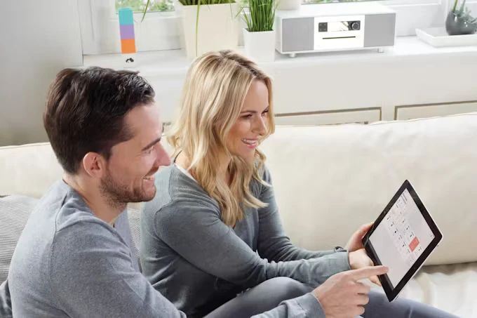 Ein Mann und eine Frau sitzen auf dem Sofa und konfigurieren am Laptop Einstellungen. 