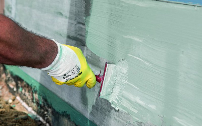 Handwerker pinselt flüssigen Baustoff an eine Wand