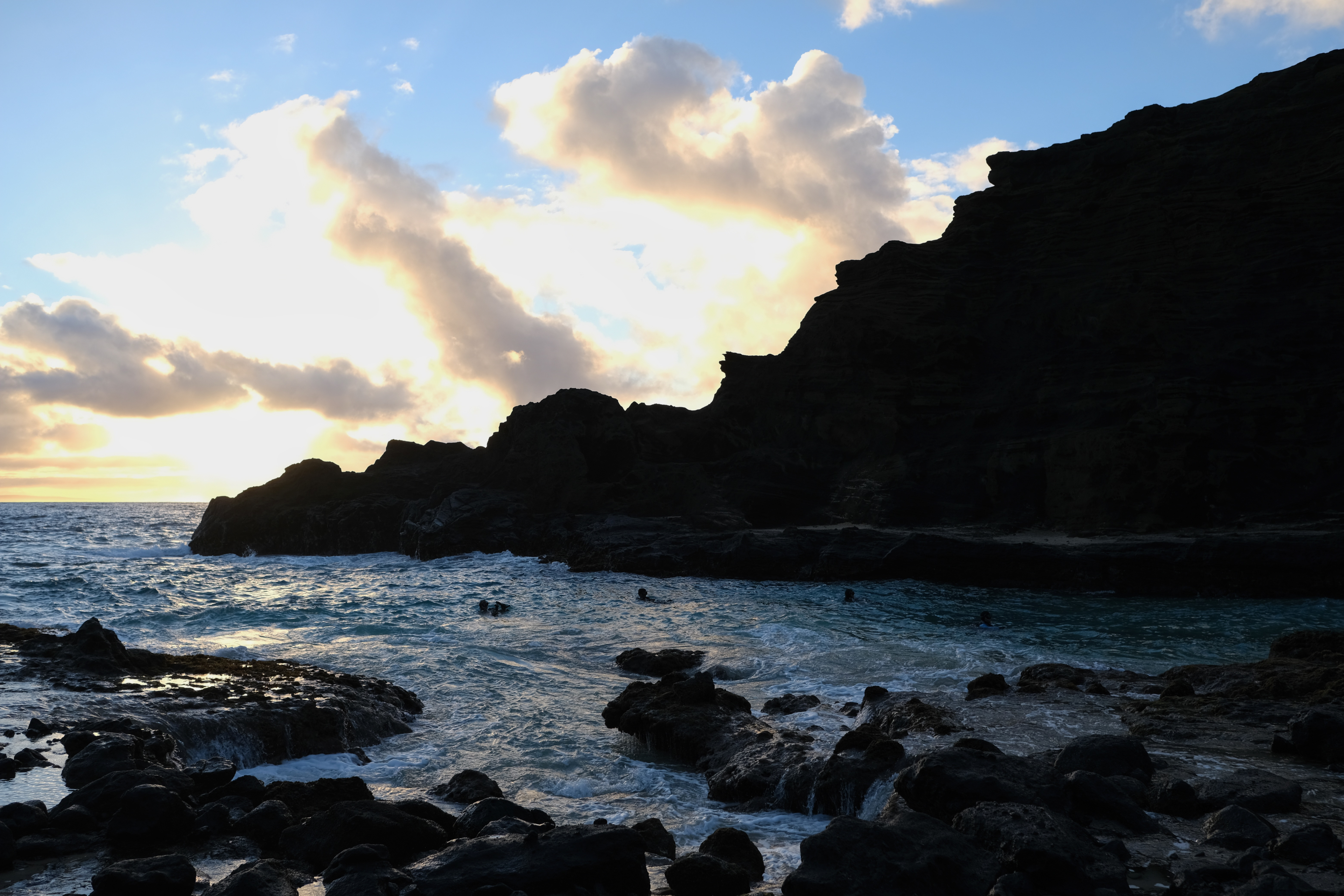 Four scuba divers slowly swimming out of a cove next to the Halona Blowhole at sunrise.