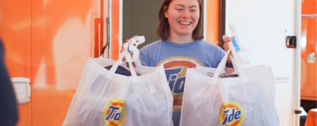 A woman handing out two bags of clothes cleaned with Tide