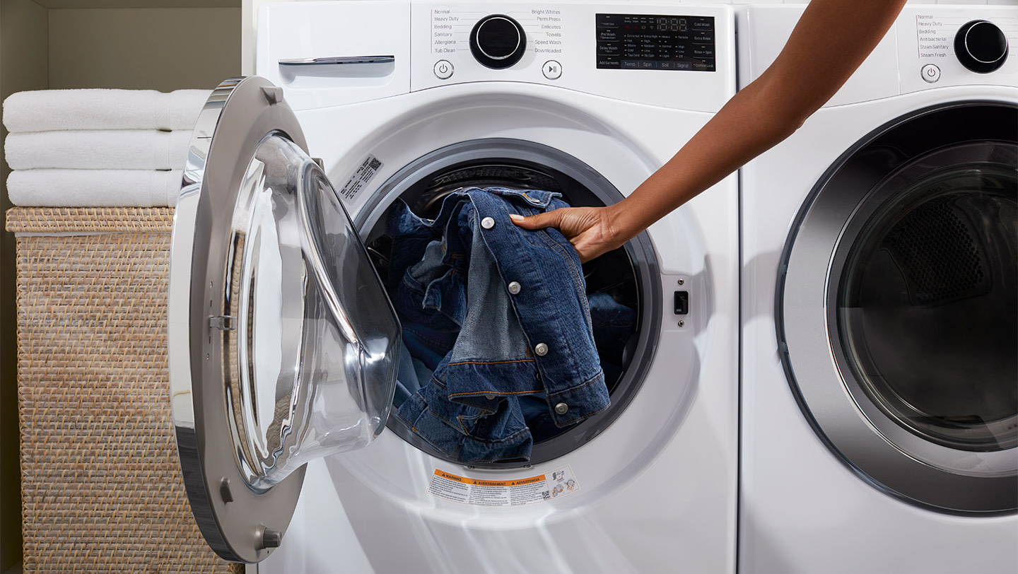 A person placing a denim jacket into the drum of a washing machine