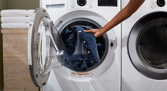 A person loading a denim jacket into the drum