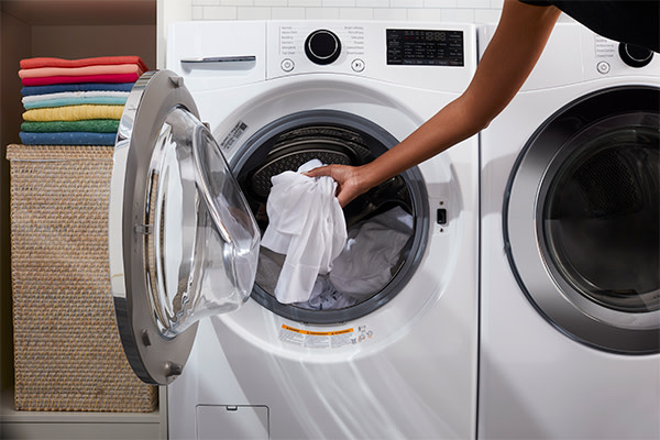 A person loading white clothes into the washing machine drum