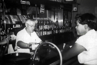 Black and white photo of Morris Hoptman serving a drink to a patron in Jake's Bar.