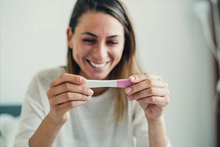Femeie care ține în mână un test de sarcină.

