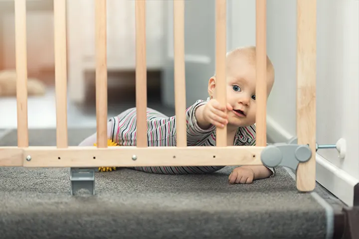 Bebeluș care se târăște în fața unor balustrade din lemn.
