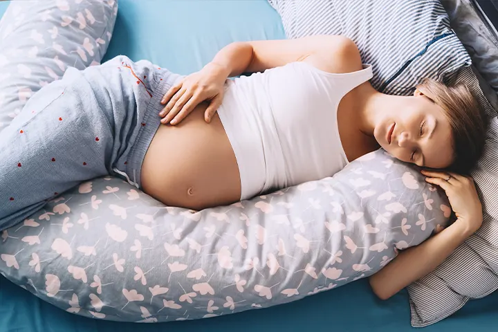 Femeie însărcinată dormind, așezată pe o pernă de sarcină.
