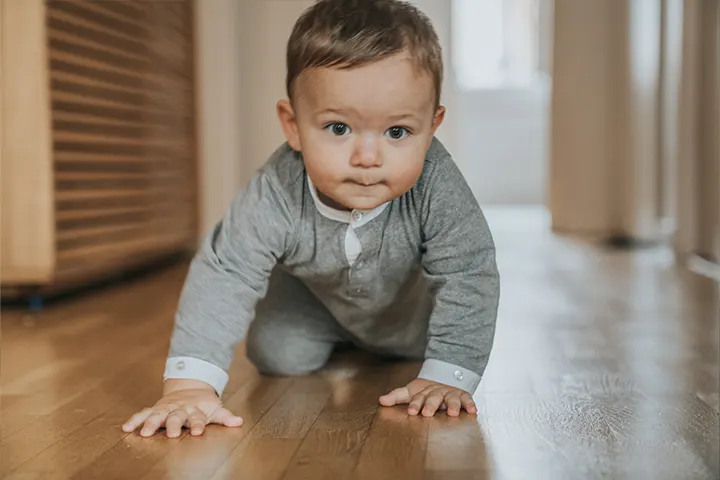 Bebeluș care se târăște pe o podea de lemn.

