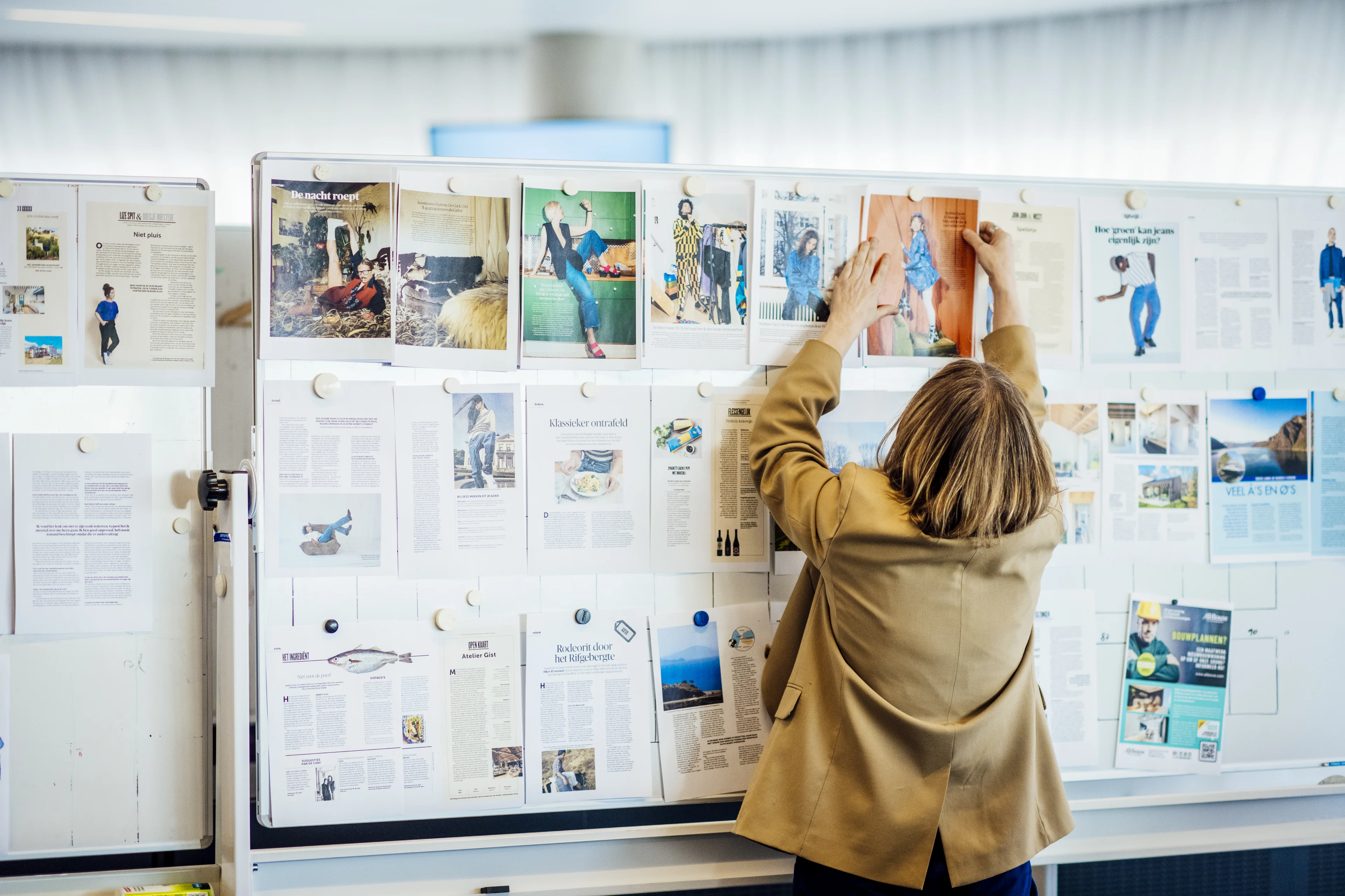 Vrouw hangt magazinecover tussen andere covers aan whiteboard