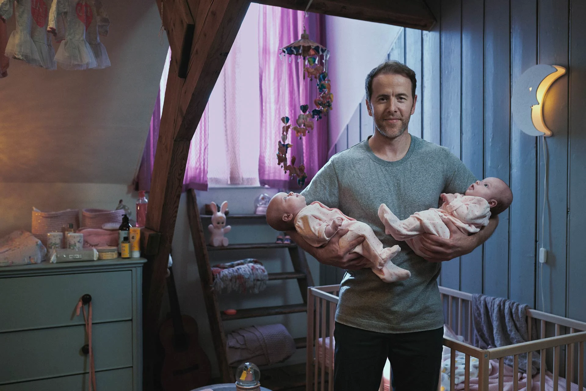 Man houdt twee babies vast in kinderkamer