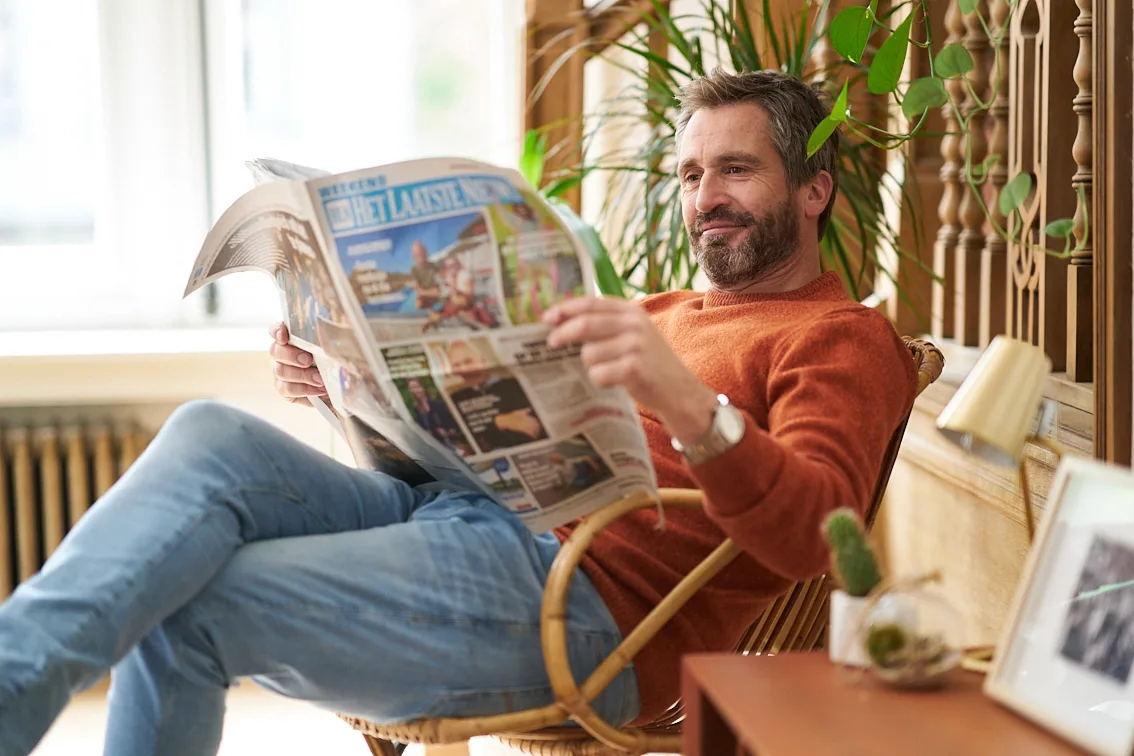 Man sitting in chair reading the newspaper Het Laatste Nieuws