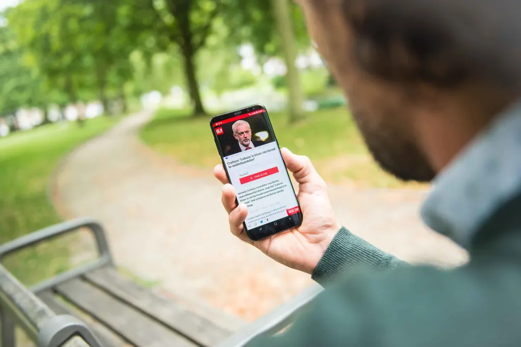 Man holds mobile phone on which he reads hln.be