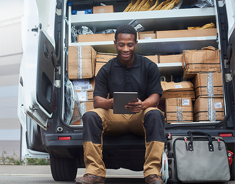 A service engineer sat at the back of his van using a digital tablet outside a building