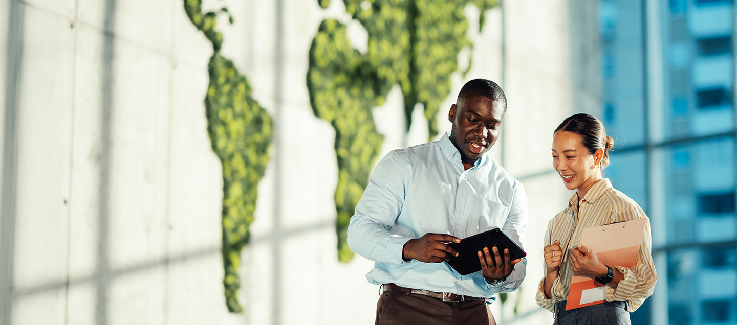 Man and woman looking a tablet in front of a wall with a map of the world in green
