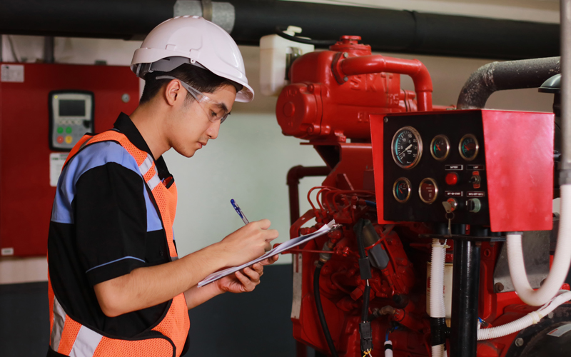 Man with hardhat and clipboard recording gauge measurements in boiler room 