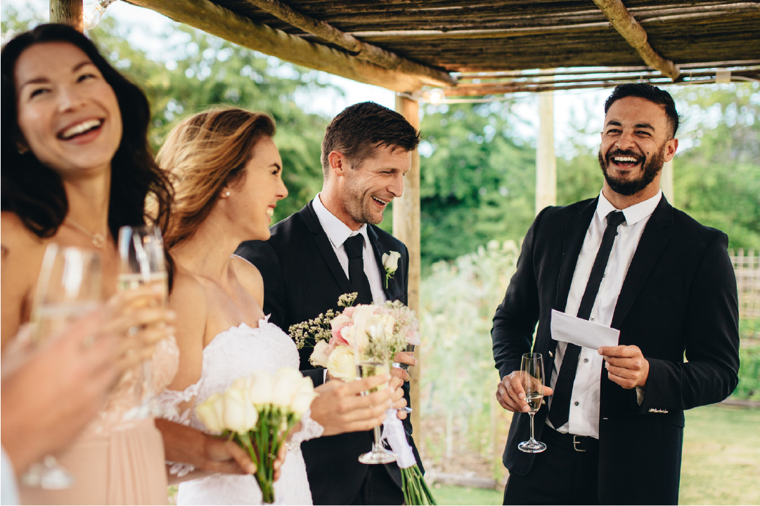 A gentleman holds a piece of a paper smiling next to a newly wedded couple, indicating he is delivering a wedding blessing.