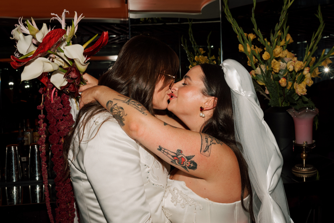 Couple sharing a kiss at their wedding, surrounded by floral arrangements with red and white flowers and yellow roses.
