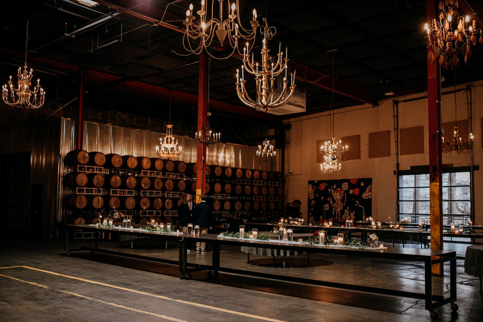Elegant winery event space with wooden barrels, crystal chandeliers, and long tables set for a formal dinner gathering.