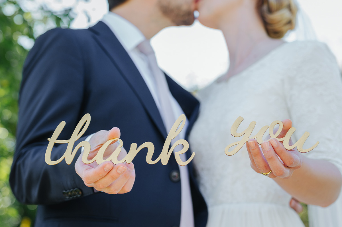 A pair of newlyweds are captured holding the words “thank you” while sharing a kiss, perhaps before practicing their wedding thank you card wording skills.